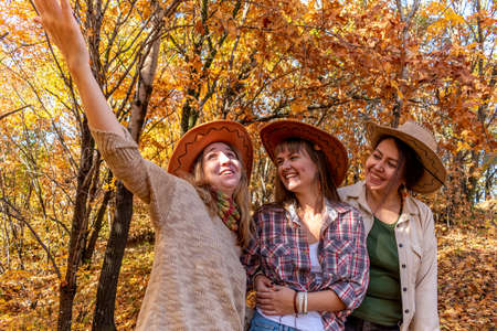 Three diverse female friends in cowboy hats are standing in the autumn forest. female friendship. outdoors. Cheerful person.の写真素材