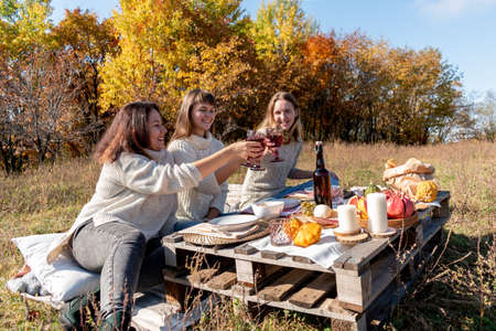 Three friends had a picnic in the autumn field. 3 young women beautifully eat and drink wine. Girl friend concept. autumn forest.の写真素材