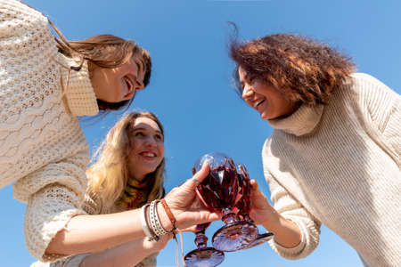 Three diverse girlfriends are having fun and hugging. blue sky background. outdoors.