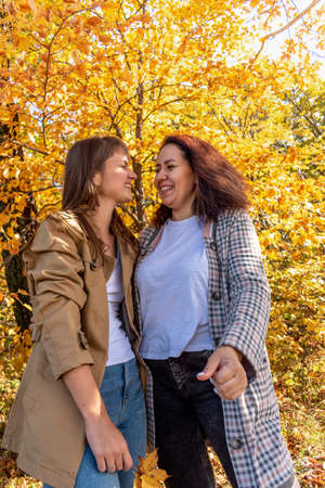 Two diverse female friends are chatting and hugging while standing in autumn forest. female friendship. outdoors. Cheerful person.の写真素材