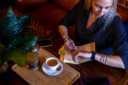 Young woman in business suit sits a cafe and looks at her smart watch. Lunch break. Herbal tea is soothing. health concept.の写真素材