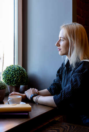 Woman a business suit holds a phone in her hand and looks out the window. Lunch break. office worker.の写真素材