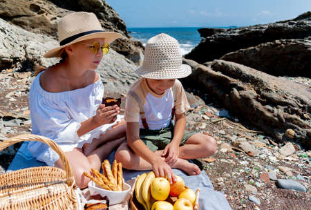 Boy and the girl tripled a picnic on the seashore near the rocks. Picnic basket. summertime. Brother and sister familyの写真素材
