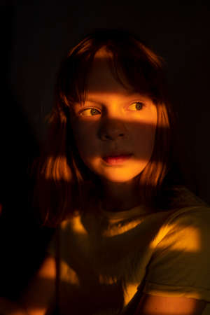 Young teen girl is sitting on the stairs with light and shadows from shutters or blinds. Little girl...