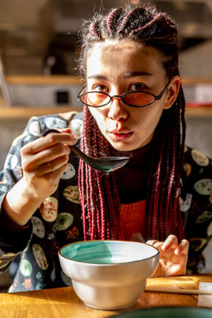 Young Asian woman eating miso soup in a cafe. Variety of girls in the city. Interior of the Japanese...