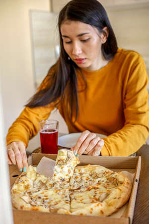Young Asian woman eats a pizza ordered from an app. food delivery. Vegetarian food. Diverse girlの写真素材