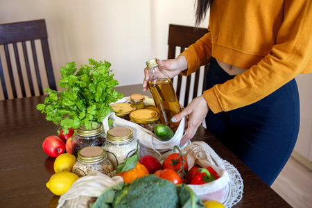 Young Asian woman takes out an olive oil from a grocery bag. Reusable package. Zero waste. Vegetarian woman. Conscious consumption.の写真素材