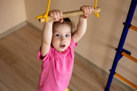 Little girl in a pink T-shirt Holds her hands on the crossbar. playground. home interior. exercise