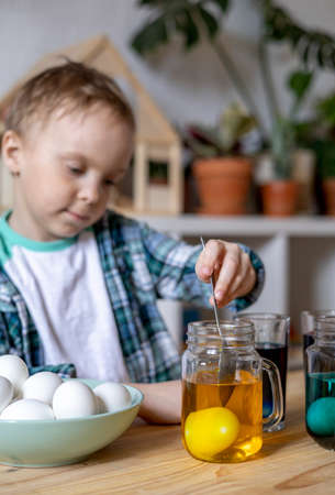 Cheerful little boy paints eggs with food coloring. Easter holiday. rainbow color. Concept of preparing for a party.の写真素材