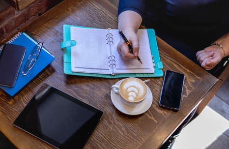 Senior woman write in notebook while sitting by the window in a small cafe. business meeting. Mature...