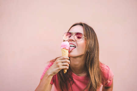 Sexy model girl in pink t-shirt licking strawberry ice cream on pink background.の写真素材