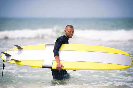 Young and fit surfer with yellow surfboard on a sunny summer day. Vacation outdoor activity.の写真素材