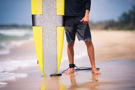 Fit surfer man holding yellow surfboard longboard on the sunny beach showing a Hawaiian shaka sign....