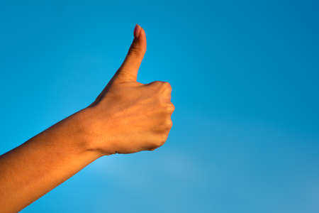 Female right hand giving thumb up like concept isolated on blue sky background.
