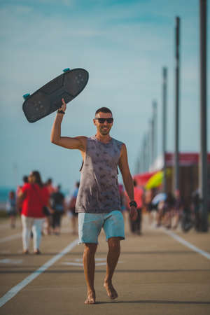 Happy carefree sporty man enjoying life and walking with longboard in his hand on sunset. Summer activities conceptの写真素材
