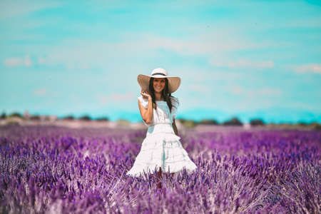 Young beautiful brunette model in white hat and dress standing in french lavender field on sunny summer day.の写真素材