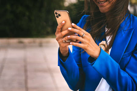 Happy smiling business woman in blue blazer using smartphone. Professional female manager reading information in internet. Typing message or shop online or checking mobile application or social mediaの写真素材