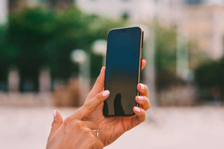Closeup of beautiful womans hands with neat pink manicure holding smartphone with black screen. Texting message or using mobile phone to check social media or unlocking deviceの写真素材