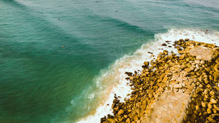 Rocky pier or breakwater. Beautiful calm green ocean with surfers. Drone photo. Aerial view. Costa Da Caparica Portugalの写真素材