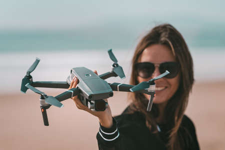 Cute modern lady pilot holds drone in her hand. Outdoors hobby. Focus on the drone.の写真素材