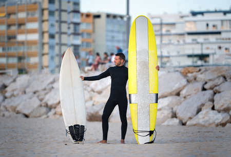 Portrait of surfer in black zipless surfing wetsuit trying to choose longboard or shortboardの写真素材
