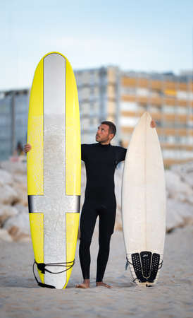 Portrait of young surfer in black zipless surfing wetsuit trying to choose longboard or shortboard in Costa Da Caparica, Portugalの写真素材