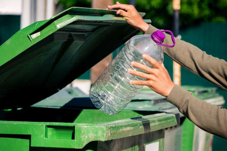 Man throwing out big plastic aqua bottle in to green garbage container. Used empty large plastic bottle.の写真素材