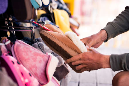 Man choosing warm brown home slippers in the shop. Buying slippers for winter. How to choose...