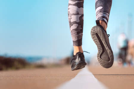 Slim woman athlete running at road. Runner feet running on road closeup on shoeの写真素材