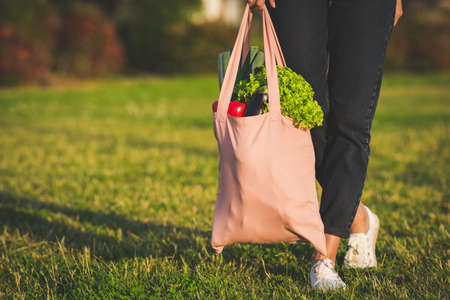 Young woman holding eco reusable textile grocery bag with fresh bio vegetables.の写真素材