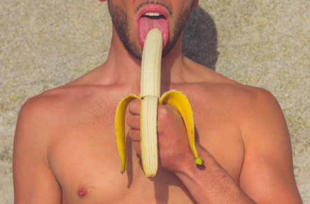 Close up of young man eating half-peeled yellow banana. Lesbian, gay, bisexual, transgender community rights support.の写真素材