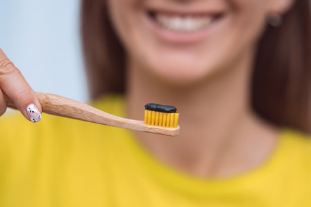 Close-up of smiling woman holding eco friendly bamboo toothbrush with black charcoal toothpaste near her mouth.の写真素材