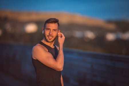 Young healthy athletic man listening music through wireless headphones during workout. Healthy...