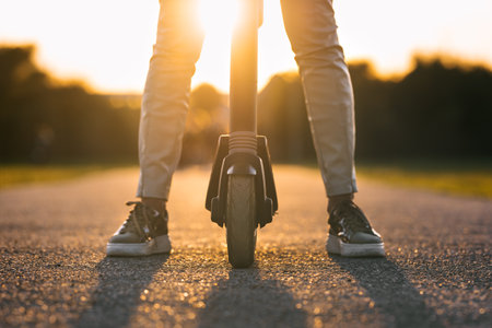 Close up of stylish woman riding electric kick scooter at sunset. Electric eco transportationの写真素材