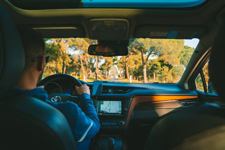 Young man driving Toyota car at sunset. Man using navigation system while driving a car. Lisbon,...