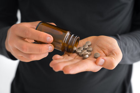 Close up of man hands taking iron supplements from the jar to treat iron deficiency anemia. Medicine to cure chronic blood loss.の写真素材