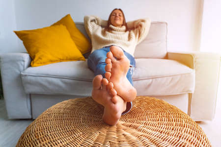 Calm young woman relaxing on grey sofa at home on a bright morning. Female enjoying lazy weekend or vacation. Carefree lady resting at home. Day off work conceptの写真素材