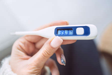 Closeup of woman hand with a medical thermometer with high body temperature 39.3