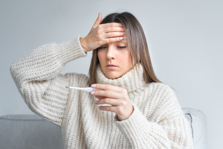 Sick unhealthy woman with fever measuring temperature with a medical thermometerの写真素材