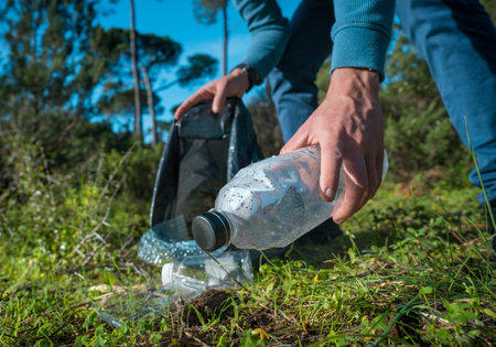 Man cleaning-up the forest of plastic garbage. Nature cleaning. Volunteer picking up a plastic in the woods. Green and clean nature. Plastic awareness activism and ecology conceptの写真素材
