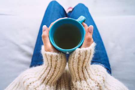 Woman in woolen cozy sweater warming cold hands with a mug of hot tea. Woman holding cup of tea.の写真素材