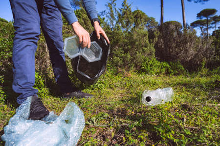 Man cleaning-up the forest of plastic garbage. Nature cleaning. Volunteer picking up a plastic in the woods. Outdoor trash and rubbish. Green and clean nature. Plastic awareness activism and ecology.の写真素材
