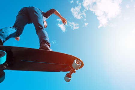 Skateboarder in action. Man riding on a longboard outdoors on sunny summer day. Blue sky background. Concept of extreme sport active lifestyleの写真素材