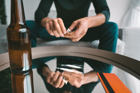 Addicted junkie man drinking beer and ready to sniff cocaine lines from mirror through rolled dollar banknote. Narcotics and alcohol addiction concept. Bad habits.の写真素材