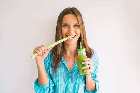 Healthy detox vegan diet. Young beautiful woman eating a stick of green organic celery and drinking...