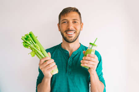 Healthy detox vegan diet. Young attractive smiling man green organic celery and fresh homemade celery juice from in a glass bottle. Healthy dieting eating and drinking lifestyleの写真素材