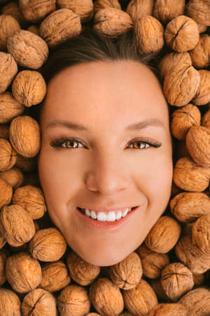 Happy woman face with perfect on a walnuts background. Eating nuts. Healthy vegetarian protein and...