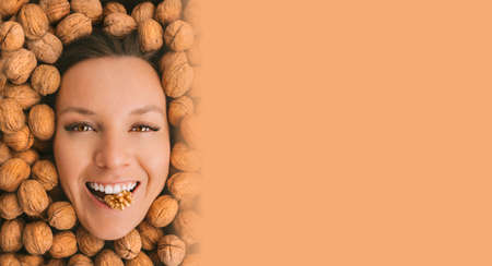 Happy woman face with perfect smile on a walnuts background with brown advertisement board for text. Eating nuts. Healthy vegetarian protein, nutritious food. Woman with strong teeth and white smileの写真素材