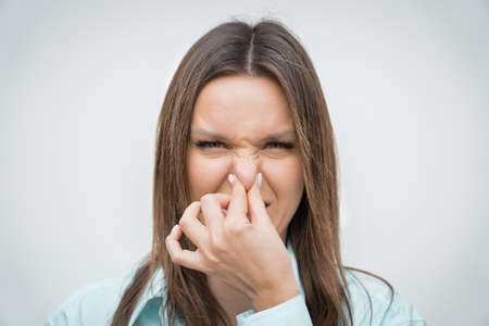 Portrait of beautiful young woman smelling something stinky and disgusting. Looking at camera with...