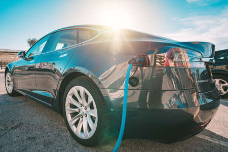 Charging Tesla electric car or EV car on parking lot with charging station. Power cable supply plugged in. Eco-friendly alternative energy. 18.03.2021, Casta Da Caparica, Portugalのeditorial素材